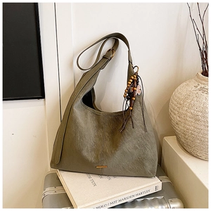 Detail van olijfgroene suède hobo tas met gouden bar en bladbedeltje op boeken