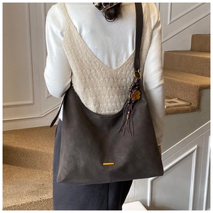 Detailed texture of a large dark brown suede hobo bag with a gold metal bar and tassel