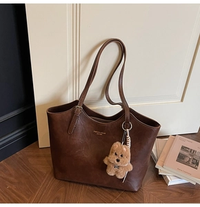 Detail of vintage dark brown leather tote bag with brand logo and cute plush puppy charm