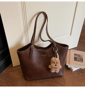 Detail of coffee brown tote bag with vintage texture and plush bear charm on strap