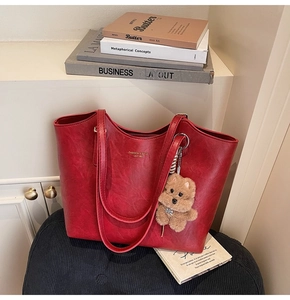 Detail view of red leather tote bag featuring a plush bear charm and minimalist branding