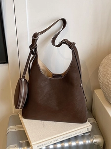 Dark brown leather hobo bag with contrast stitching and small pouch on white book