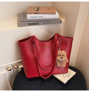 Detail of red leather tote bag with gold lettering and brown plush bear charm