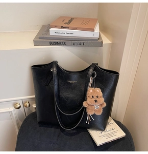 Detail of black faux leather tote bag with gold lettering and cute brown plush bear charm