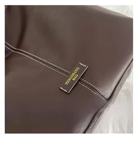Detail of dark brown leather bag showing premium white contrast stitching and gold label