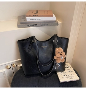 Detail of black tote bag featuring textured leather and a cute plush dog pendant charm