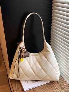 Beige quilted hobo shoulder bag with crossbody strap and decorative charms on wood surface