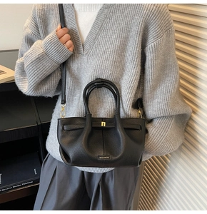 Detail of black lychee grain leather bucket bag featuring a gold buckle and metal logo
