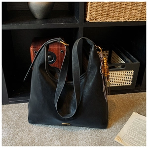 Detail of black leather hobo bag featuring golden hardware and ethnic fringe charm