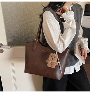 Detail of dark brown leather tote bag with gold lettering and plush bear charm accent