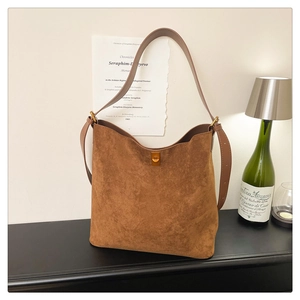 Detail of matte brown suede bucket bag featuring a golden twist-lock buckle and wide strap
