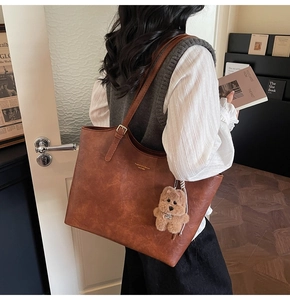 Brown leather tote bag featuring gold lettering and a plush bear pendant charm detail