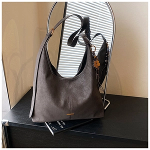 Close-up of a dark grey tote bag featuring a four-leaf clover charm and gold metal bar