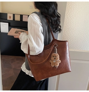 Detail of vintage brown leather tote bag with gold lettering and plush bear charm