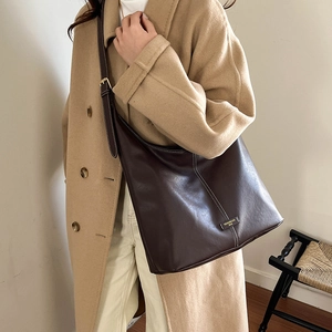 Detail view of large dark brown leather bag with white contrast stitching and metallic logo