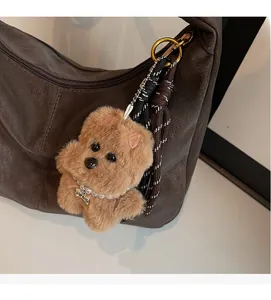 Detail of a brown plush dog charm with pearl necklace on a leather tote bag