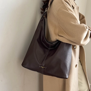 Detail view of large dark brown tote bag with contrast stitching and gold logo plate