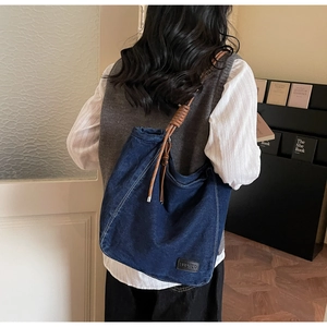 Detail of blue denim tote bag with brown braided rope knot shoulder strap and leather patch