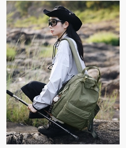 Detail of army green nylon backpack with front zipper pocket and side pockets in outdoor setting