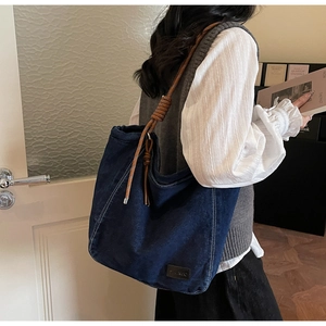 Détail du cabas en jean bleu foncé avec poignées en corde tressée et logo en cuir