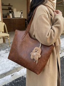 Retro brown faux leather tote bag with plush bear charm worn by a model in winter