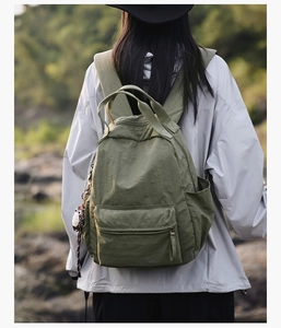 Outdoor view of an army green nylon backpack with owl charm and multi-pocket design