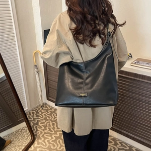 Close-up of black leather tote bag featuring white contrast stitching and gold metal logo