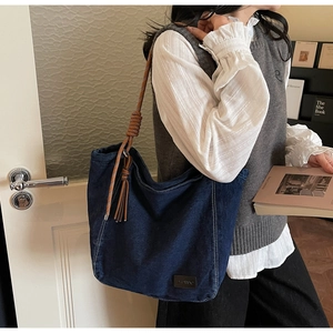 Close-up of dark blue denim tote bag featuring braided rope straps and leather tassels