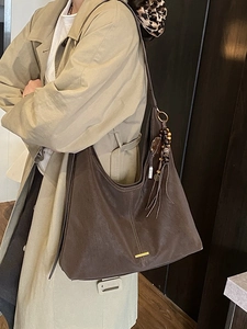 Retro brown suede tote bag with fringe charm and gold metal accent on beige coat