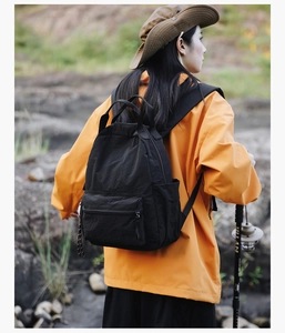 Outdoor back view of a black waterproof nylon backpack with front zipper and side pockets