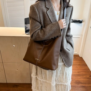 Detail of dark brown leather tote bag with vertical white stitching and metal logo