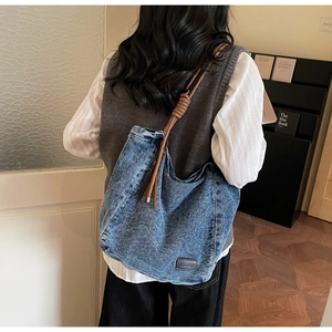 Detail of blue denim hobo bag featuring woven rope strap and brand leather patch