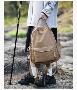 Detail of khaki outdoor backpack with owl charm and side pocket on a rocky landscape