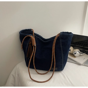 Détail d'un sac cabas en jean bleu foncé avec bandoulière en corde et couture blanche