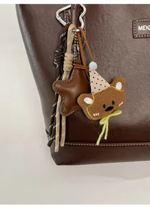 Detailed view of a brown plush bear charm and woven rope on a textured leather bag