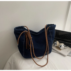 Gros plan sur un cabas en denim bleu foncé avec anses tressées et longs glands latéraux