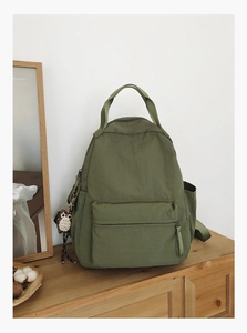 Close-up of olive green nylon backpack featuring owl pendant and front zipper pocket