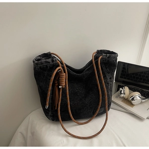 Gros plan du sac cabas en denim noir avec bandoulière en corde épaisse et pompon