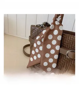 Close-up of brown woven handbag featuring decorative polka dot silk scarf handle detail