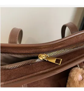 Detail of smooth gold zipper on a brown suede tote bag with plush bear charm