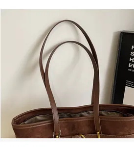 Close-up of the suede fabric, sturdy leather handles, and golden zipper detail of the tote bag