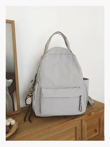 Detail of light gray minimalist backpack with cute owl charm on wooden shelf