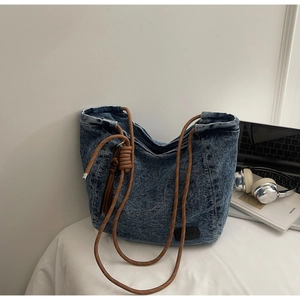 Détail du sac cabas en jean bleu avec anses en corde tressée et écusson logo en cuir