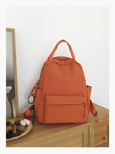 Detail of an orange lightweight travel backpack with many pockets and an owl charm accessory