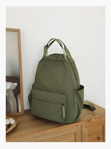 Detail of army green nylon backpack with front zipper pocket on wooden storage cabinet