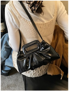 Detail of black patent leather ruched tote bag with rectangular cutout handle and strap