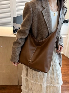 Large brown leather tote bag with white stitching shown on model in a stylish suit