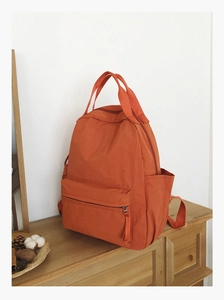Detail view of bright orange nylon backpack with side water bottle pockets and zipper compartments