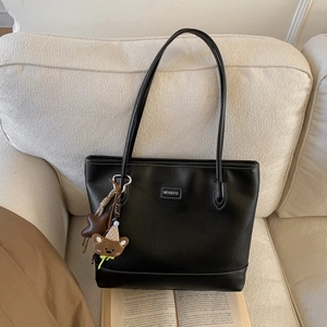 Detail of black matte leather tote bag with star charm and bear pendant on a sofa