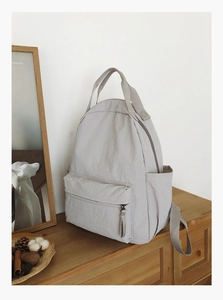 Detail of minimalist beige nylon backpack with zipper pocket and dual top handles
